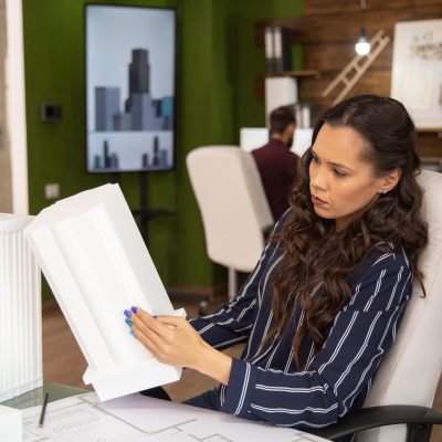 Female architect in modern office looking at 3D printed model of building she is working on