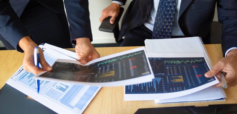 Investor and trader discussing statistic data, holding papers with financial charts and pen. Cropped shot. Broker job or trading concept