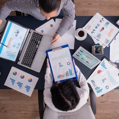 Top viewTop view of manager and employee doing teamwork in business office , looking at charts on laptop display. Finance paperwork with charts at workplace. Discusing financial plan.